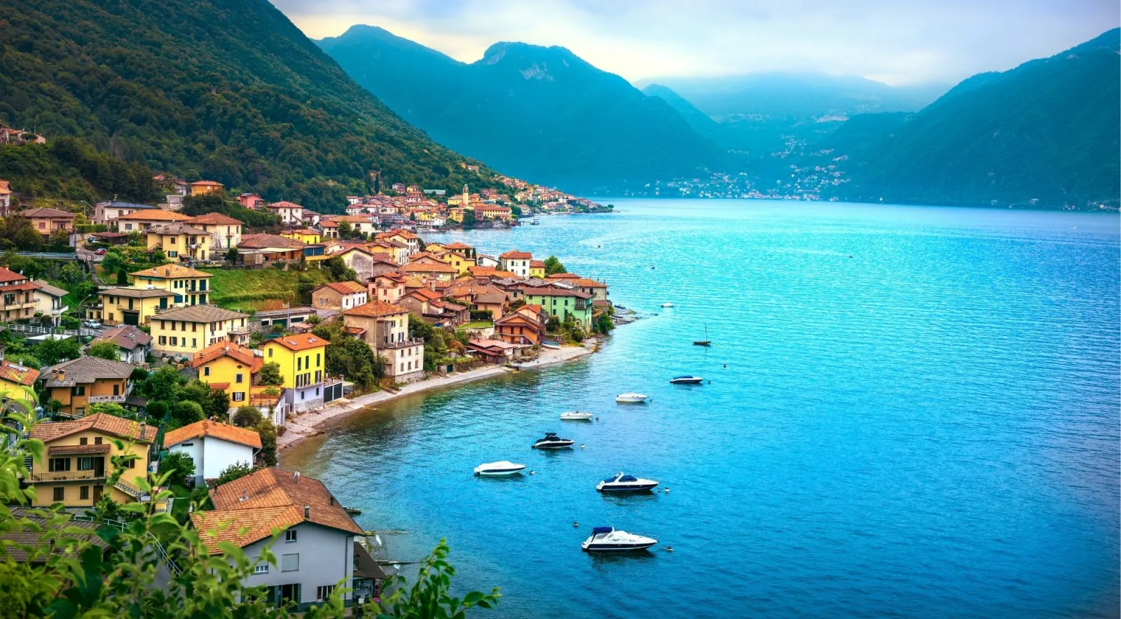 Aerial view of a Lake Como village with moored boats along its turquoise shoreline