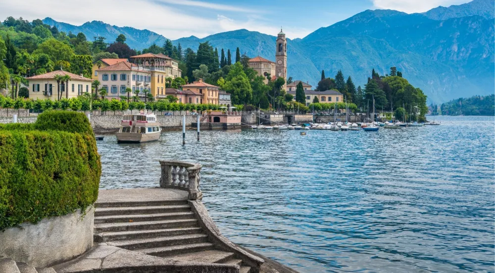 A Lake Como village promenade with a bell tower and moored boats