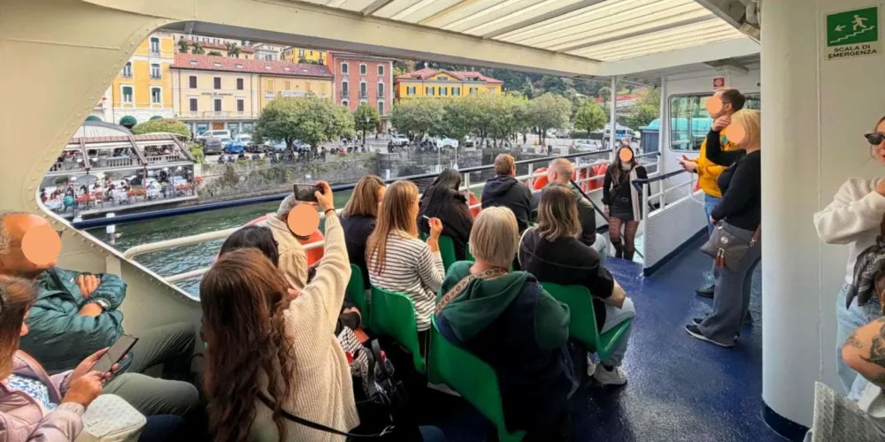 Passengers on the open deck of a Lake Como ferry approaching a lakeside town