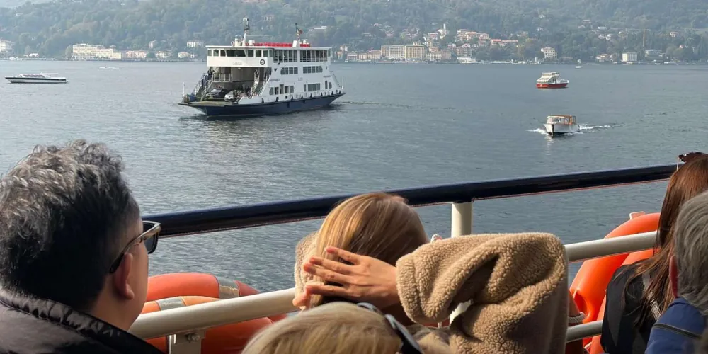 View from a ferry of a white Lake Como car ferry crossing toward the town of Como